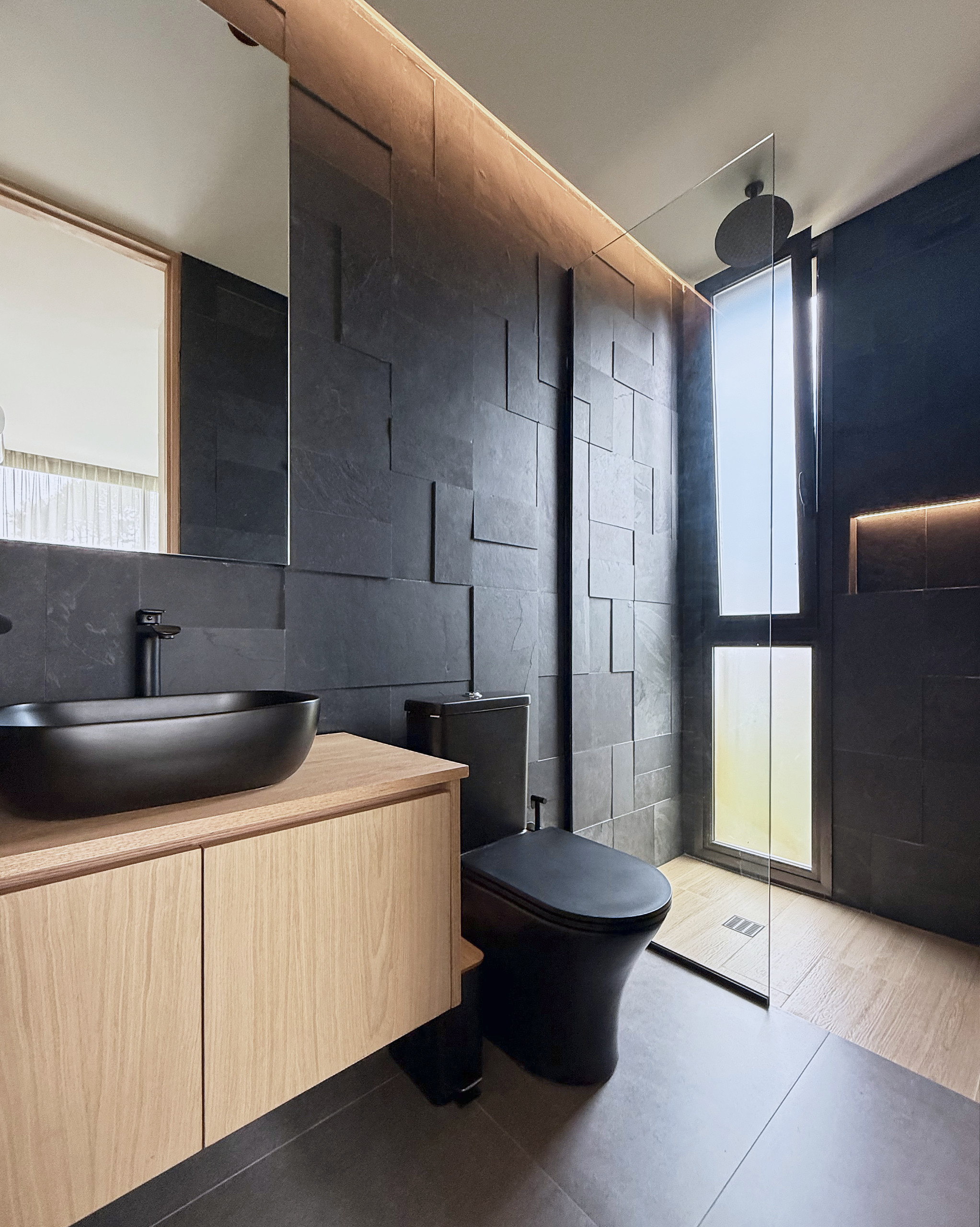 Baño con revestimiento oscuro, madera y ducha vidriada
