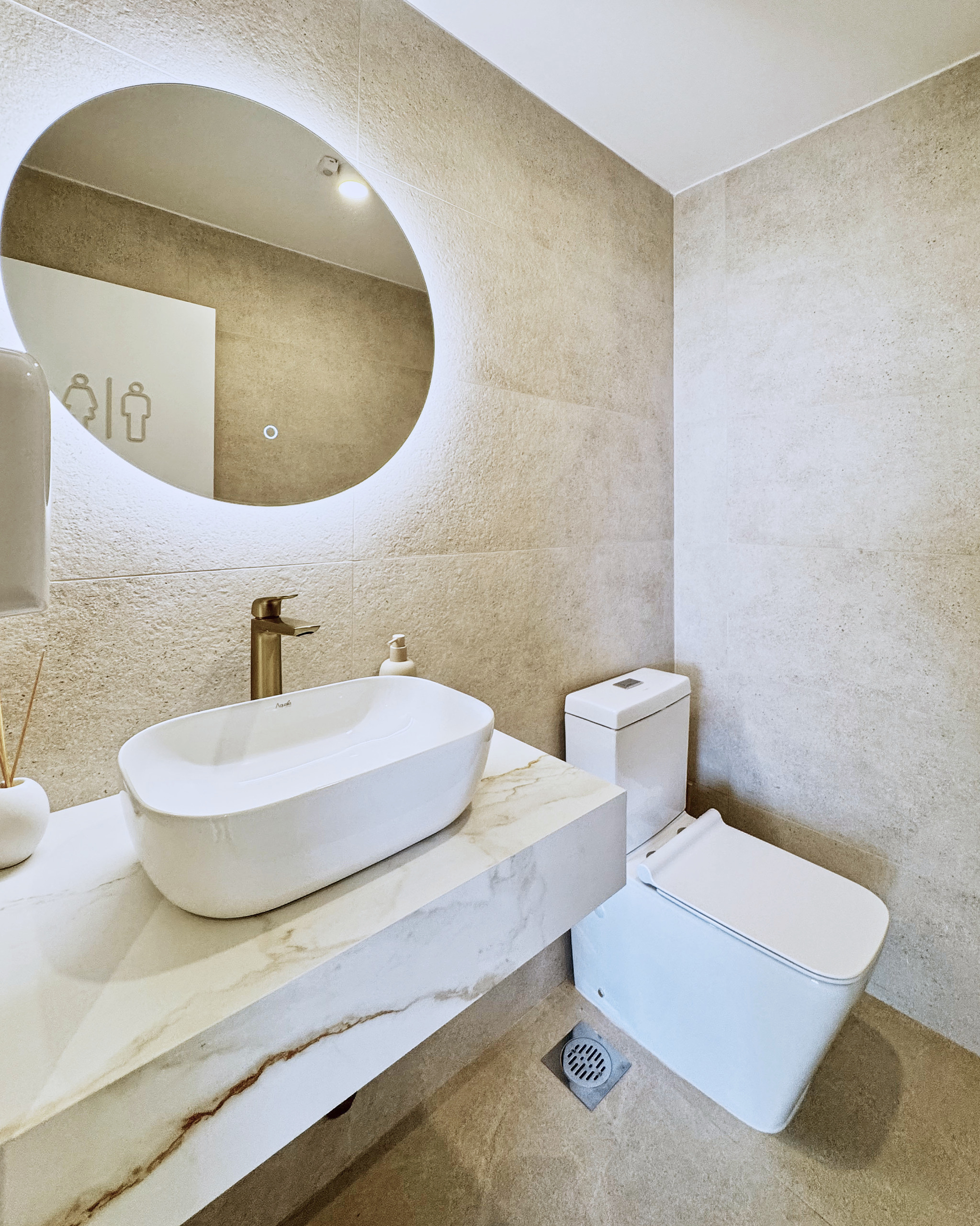Baño de Clínica Berrutti con espejo circular y mesada de piedra