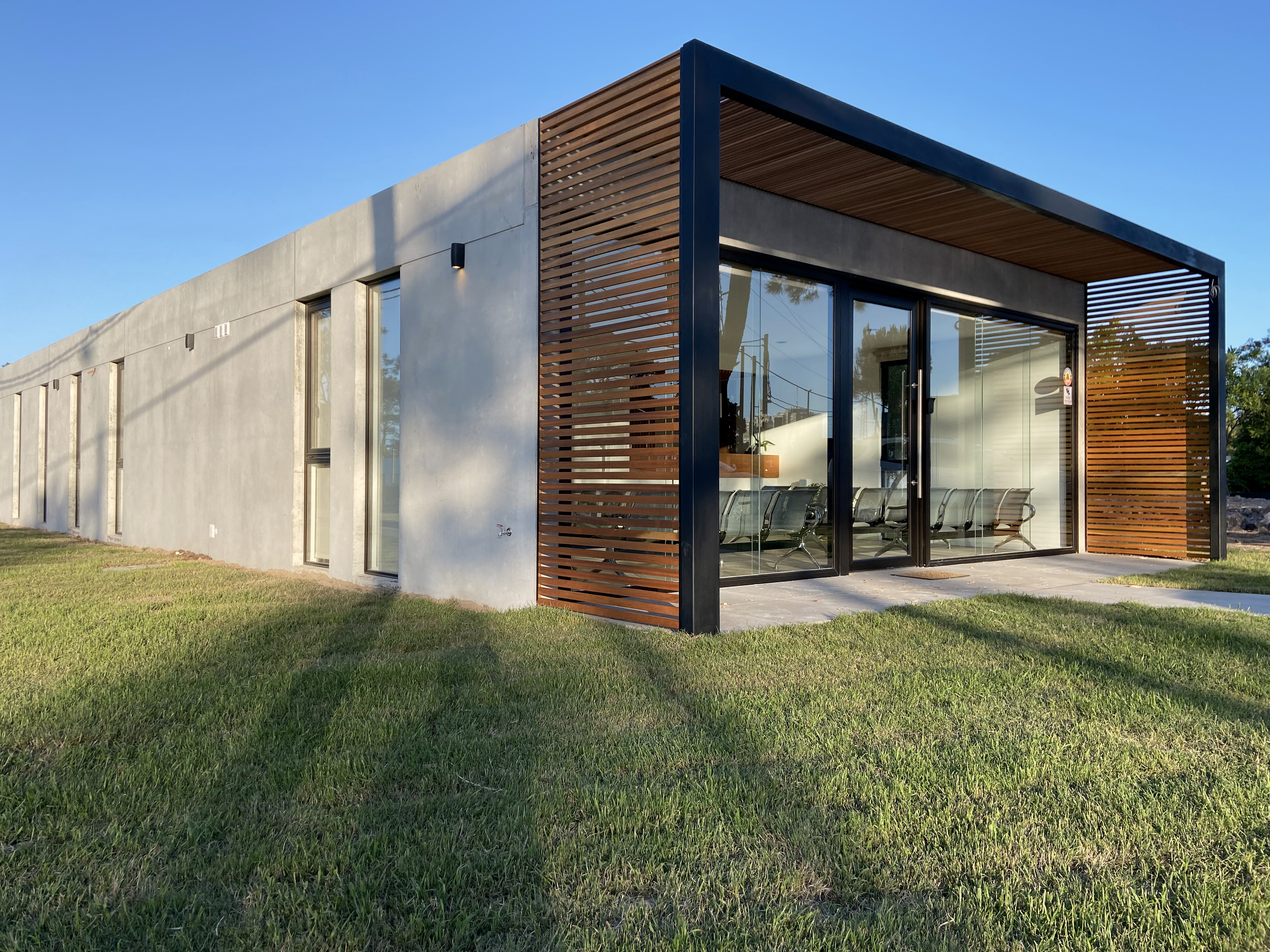 Vista exterior completa de Clínica Lumiere con hormigón, madera y grandes paños vidriados