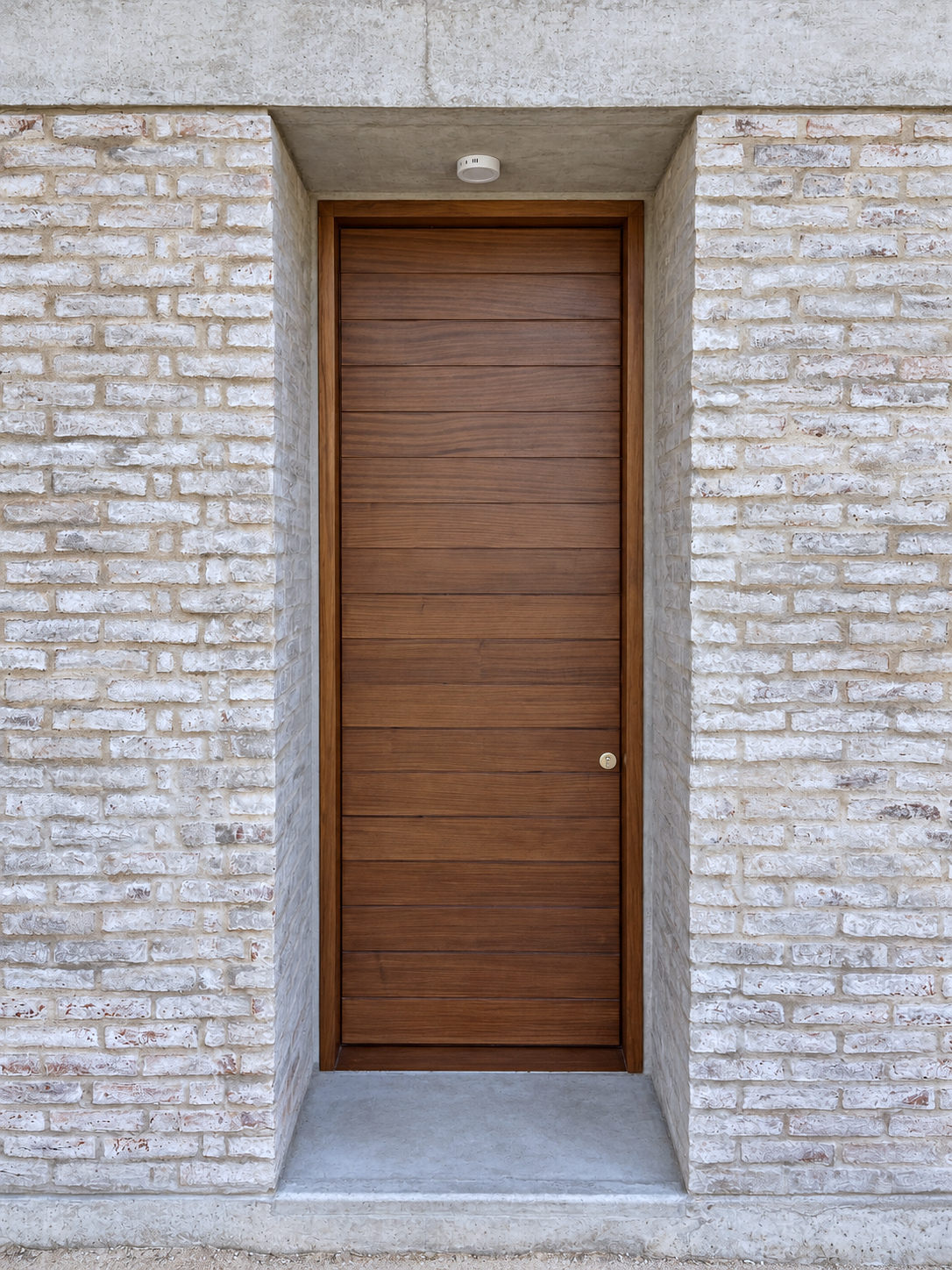 Detalle del acceso con puerta de madera y muros de ladrillo claro